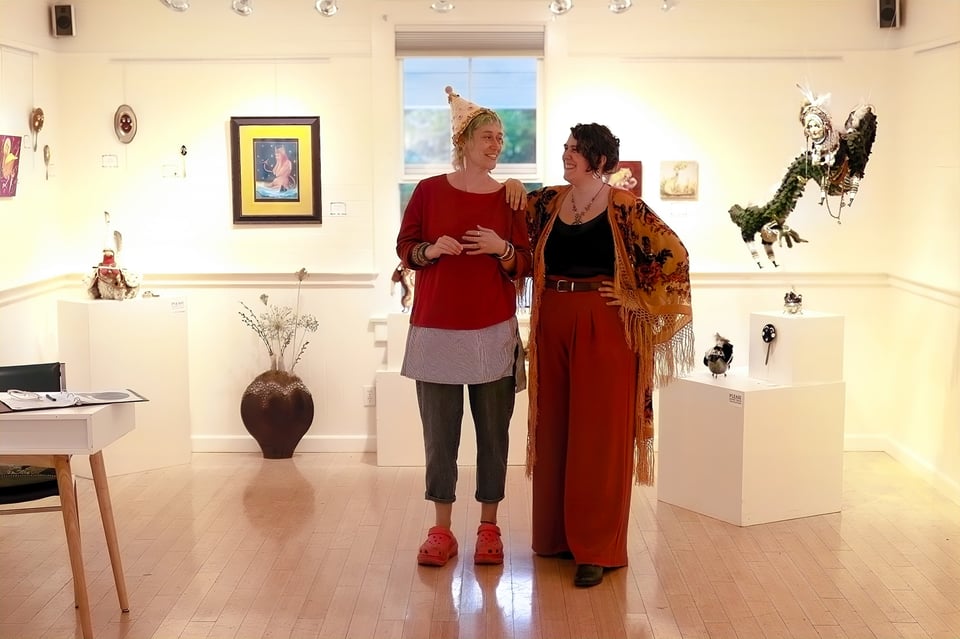 A photograph of two artists in the gallery with their artwork