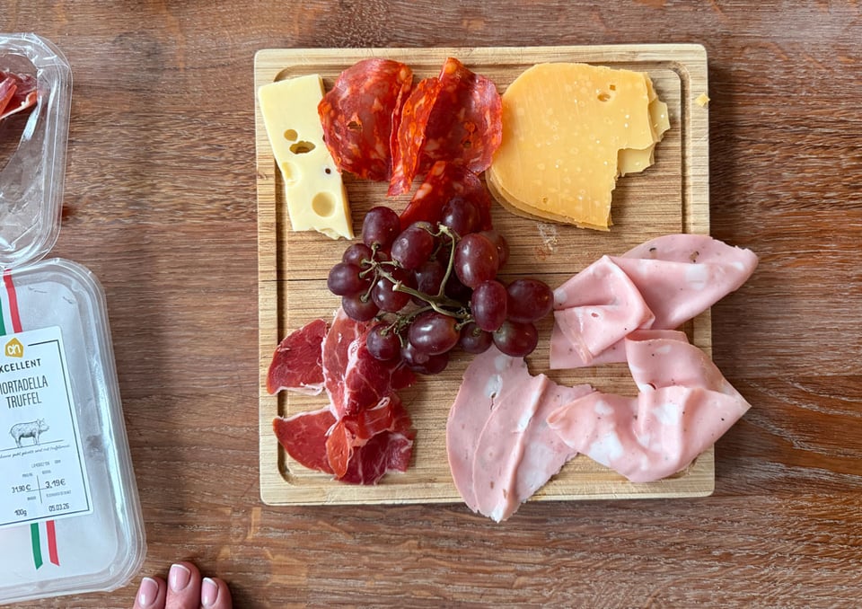 A small charcuterie board is filled with ham, bologna, salami, cheese and grapes.