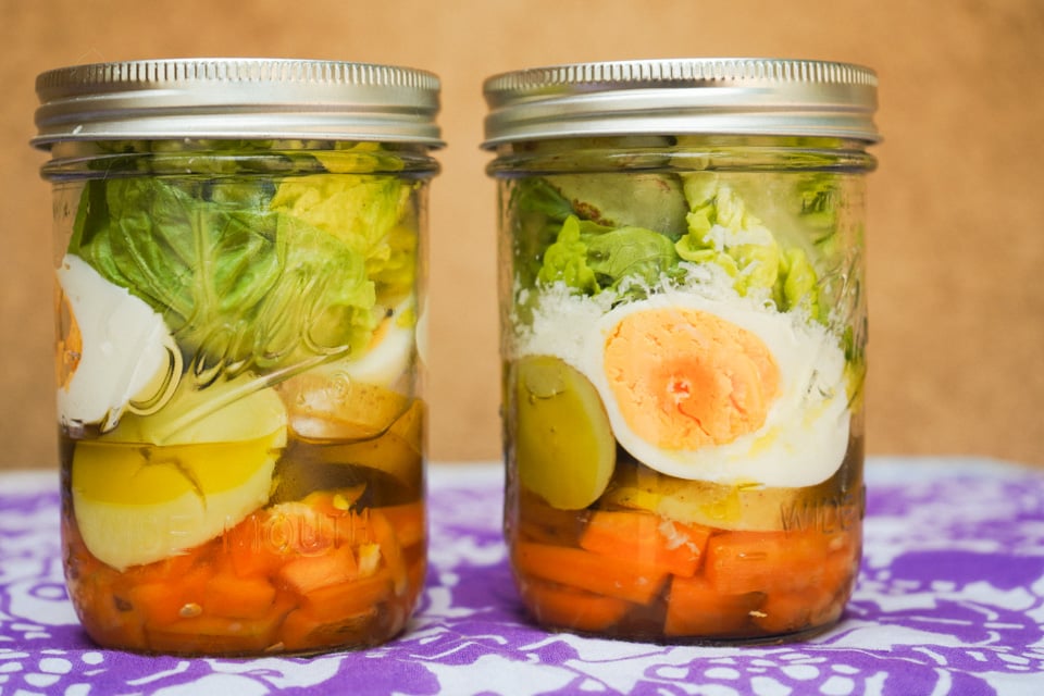 Two jarred salads made with lettuce and an egg sit on a purple tablecloth 