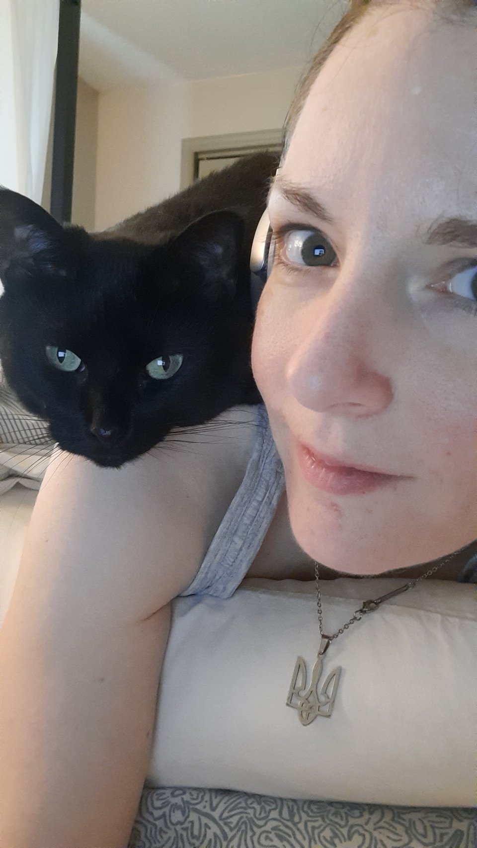 A black cat sits on a woman's shoulder and looks at the camera