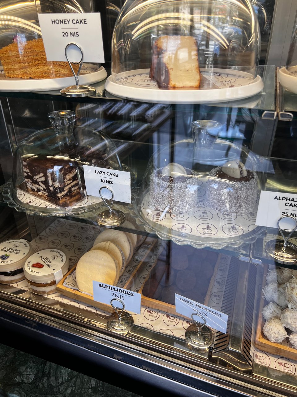 A display case in a bakery, including alfahores (spelled with ph instead of f as is typical), along with honey cake and something called lazy cake