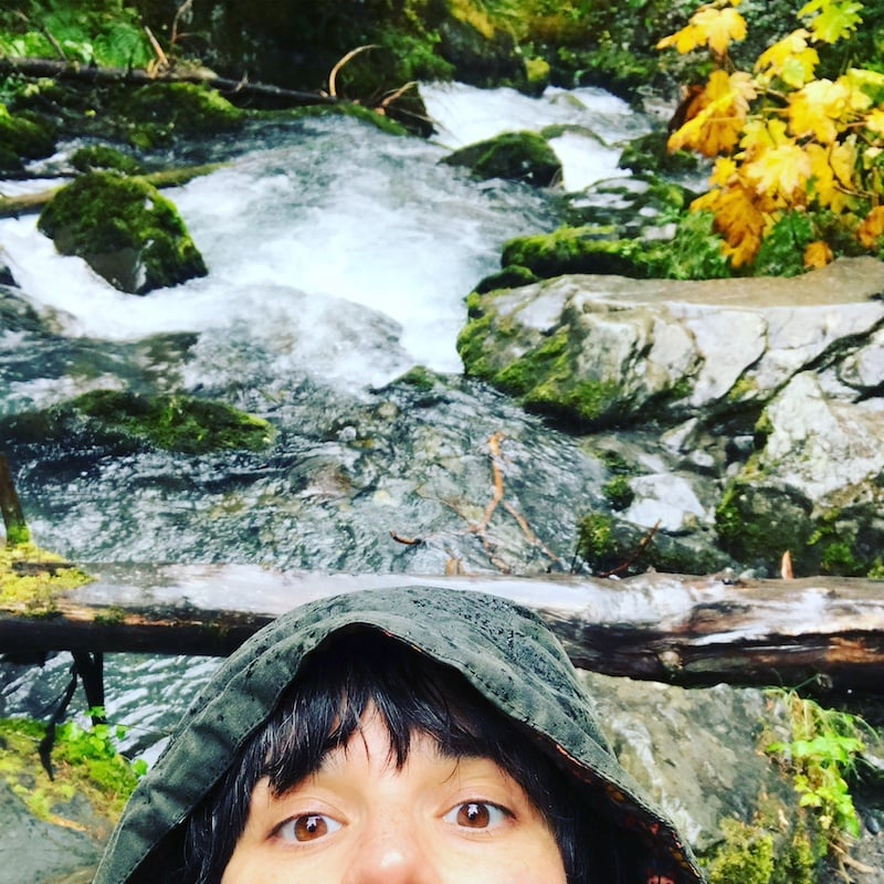 a person in a hoodie taking a selfie next to a stream