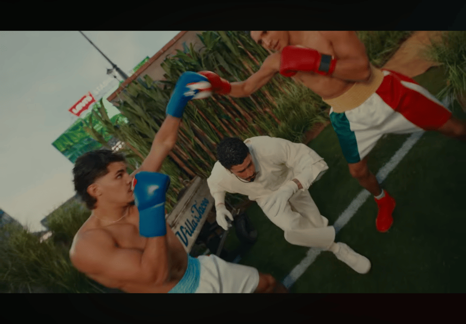 Bad Bunny dashes under the arms of boxers sparring in gloves donning the Puerto Rican flag.