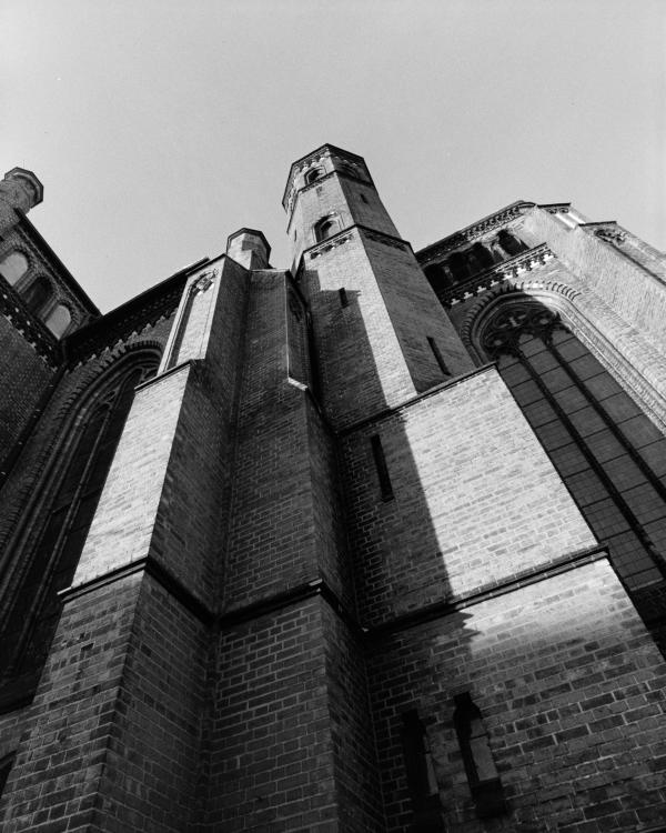 Low-angle B&W shot of the towering brick facade and spires of St. Paul's Church in Schwerin with grainy film textures.