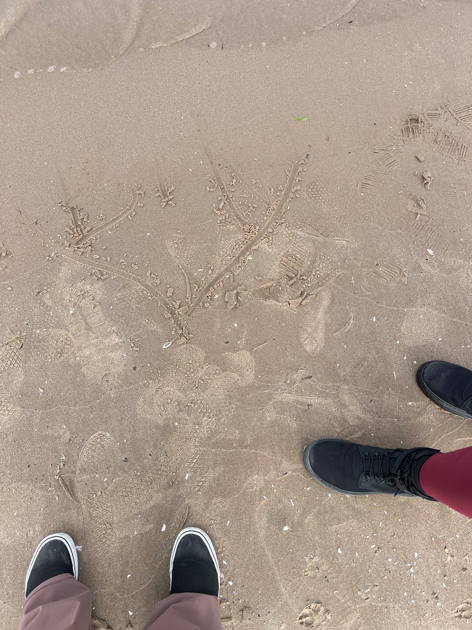 two sets of feet - one in vans, one in boots - on a sandy beach with a heart and initials half washed away