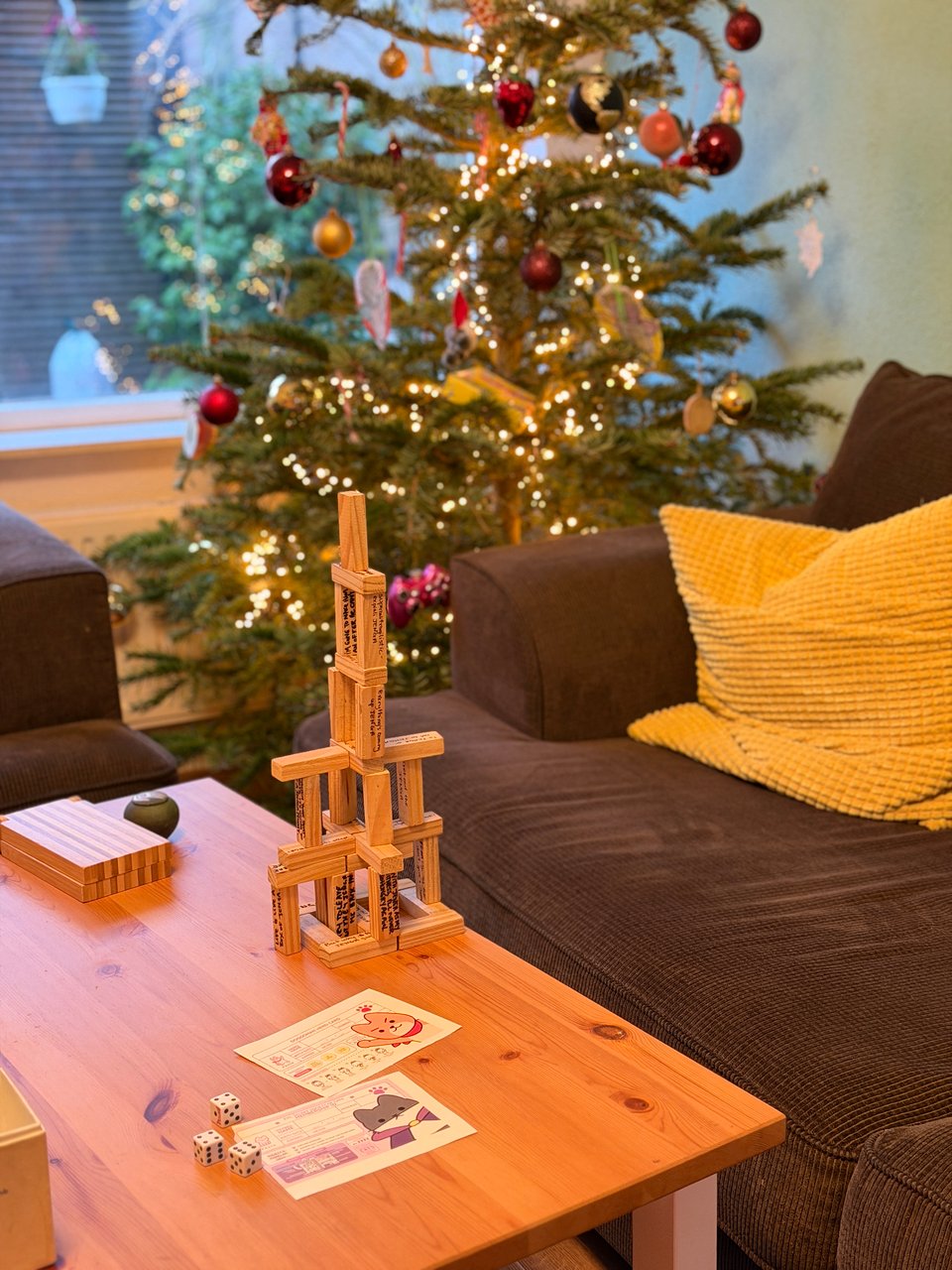 A structure made out of Jenga pieces sits on a coffee table in a living room. A decorated Christmas tree is in the background.