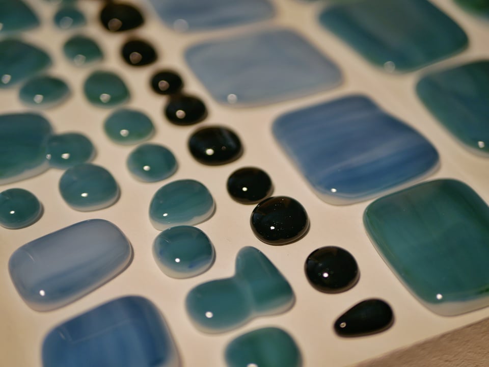 kiln shelf with black cabochons in the middle with teal and blue ones on either side