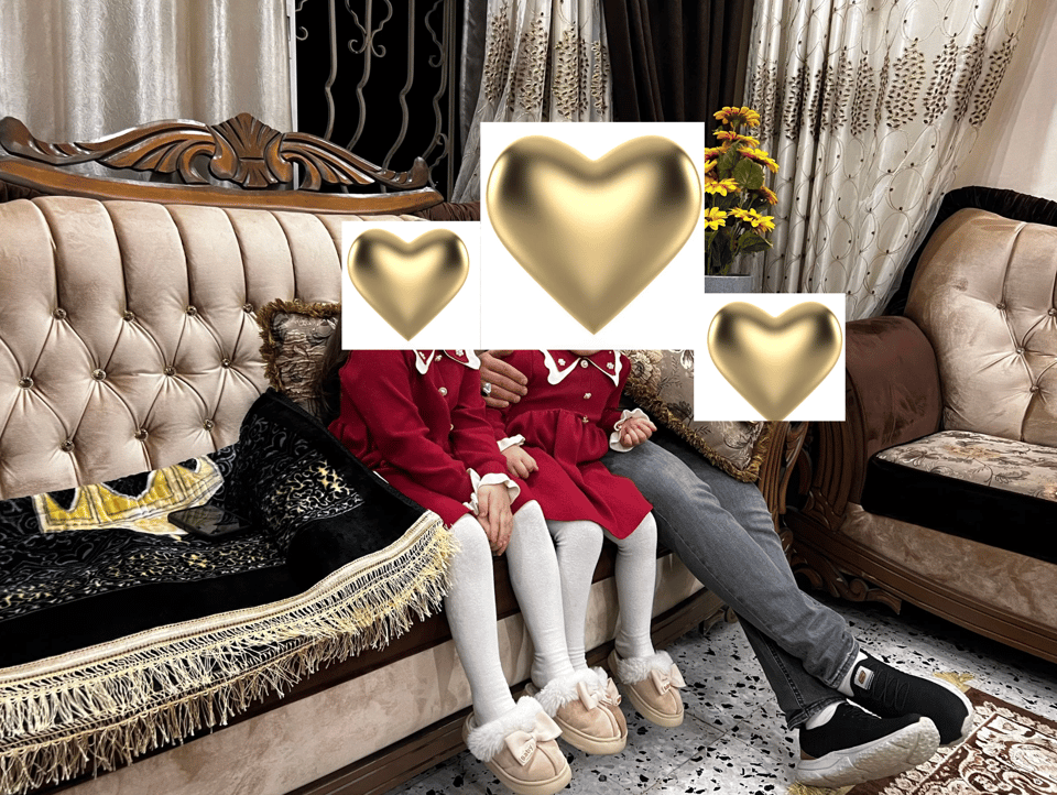 Three people sitting on an elegant sofa: two little girls in matching red dresses, white tights, and slippers with bows; and a man.  All three faces are covered with hearts