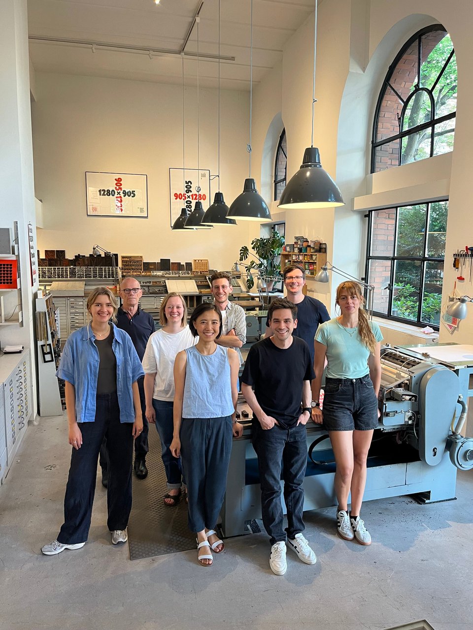 Group photo of the whole Village One team, Erik Spiekermann and Lilith standing around a letterpress printing machine, all smiling at the camera (except Erik, he looks uncharacteristically serious)