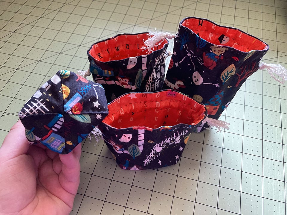 Four small Halloween treat bags with drawstring tops and boxed bottoms. The outside are black with cute animals dressed in Halloween costumes and trick-or-treating, and the insides are orange with Halloween words in a crossword puzzle style.