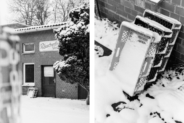 Left: B&W film shot of a brick building with a "Räucherfisch Verkauf" sign in a snowy landscape. Right: Close-up of snow-covered crates leaning against a brick wall with visible film grain.