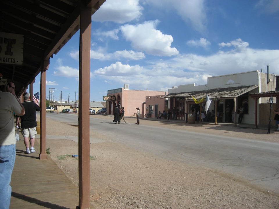A broad, dusty road, lined by old plaster buildings, with the sidewalks covered.