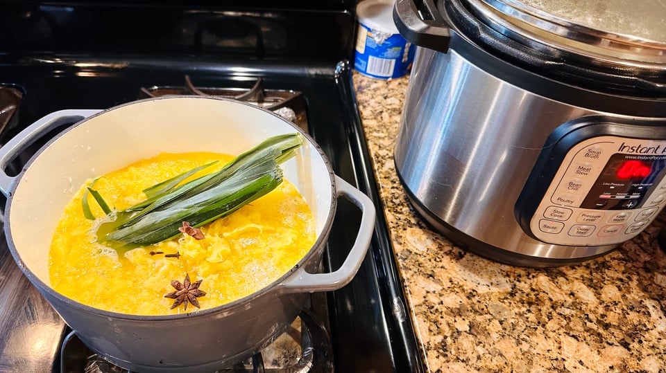 A photo of pineapple gratings in a dutch oven, being cooked down with spices and pandan leaves
