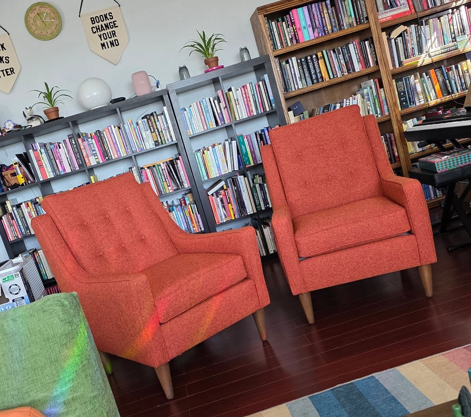 Two orange mid-century modern reading chairs in front of many full bookshelves