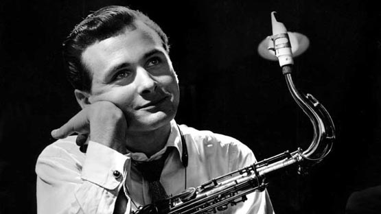 A man in a shirt and tie holding his saxophone and looking up with a smile on his face