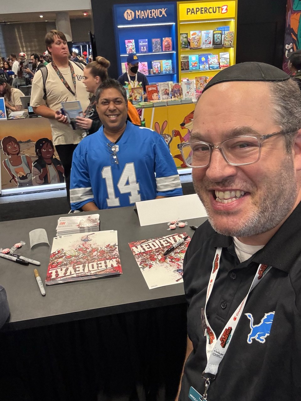 neil signing at the comixology booth ay nycc 25 talking to a fan in a detroit lions #14 shirt, the mad cave booth in the background