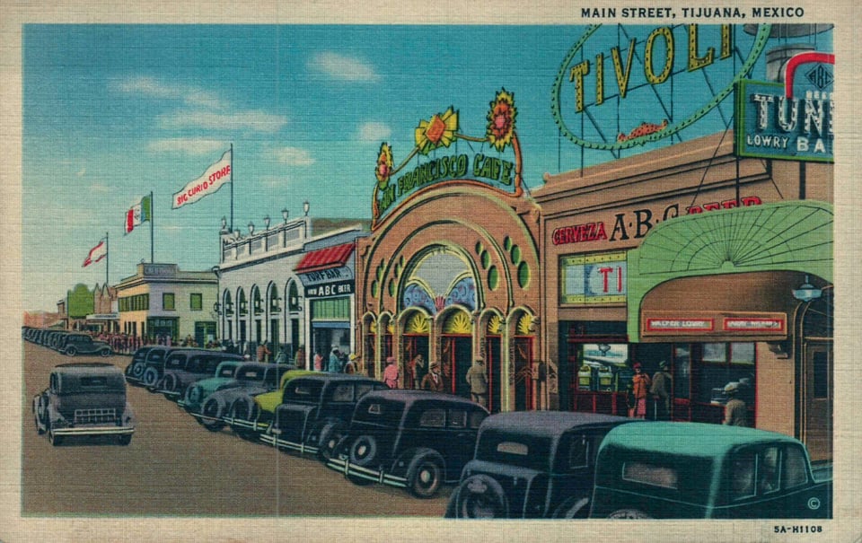 vintage postcard shows downtown Tijuana with people lined up outside bars and a full row of cars out front