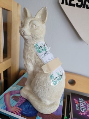 A large plastic white cat with a mailing label address to Ms. and Mrs. Elzie-Tuttle and six dollars in postage stamps