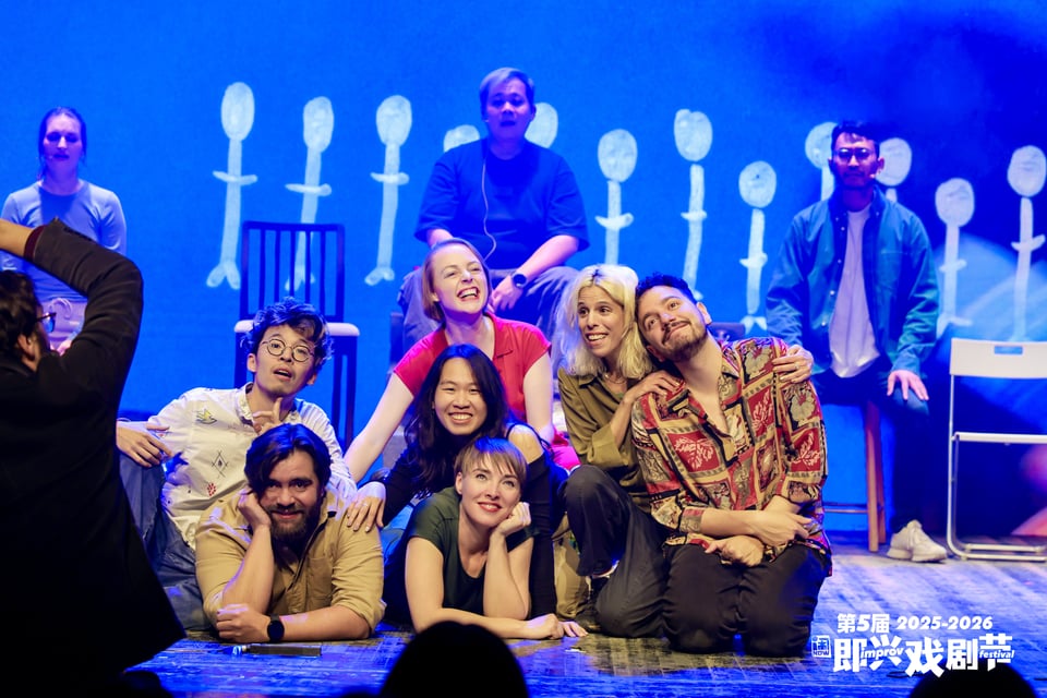 Group of performers smiling and as a group on the ground. The soundpainting is half-seen in the shot, signing something.
