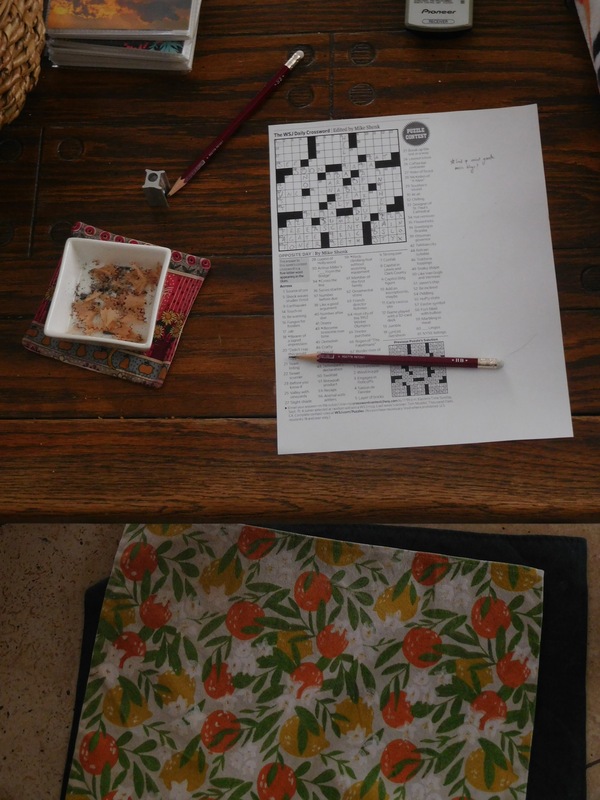 Top-down view of a coffee table with a crossword puzzle, a couple of pencils, and a little square dish filled with pencil shavings.