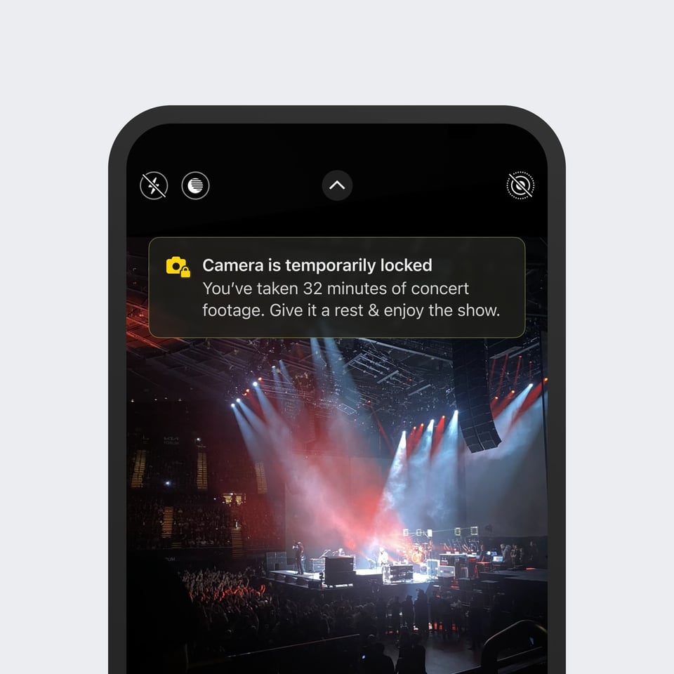 Parte superior de un teléfono móbil mostrando una imagen de un concierto con una notificación que dice, en inglés "La cámara está temporalmente bloqueada. Has grabado 32 minutos de imágenes del concierto. Descansa un poco y disfruta del espectáculo"