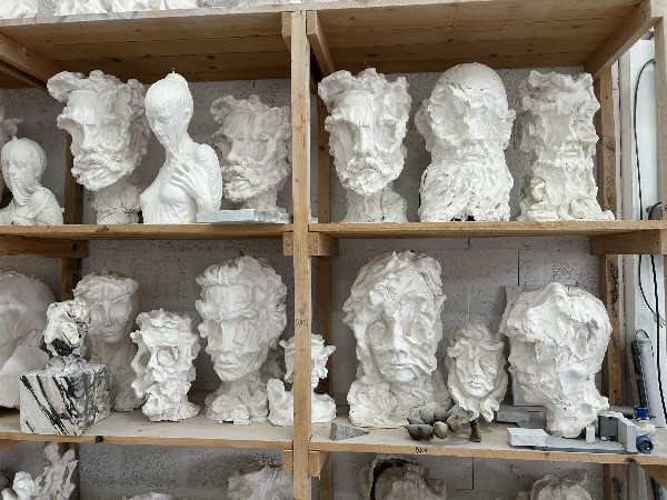 Multiple abstract white marble sculptures of heads on wooden shelves.
