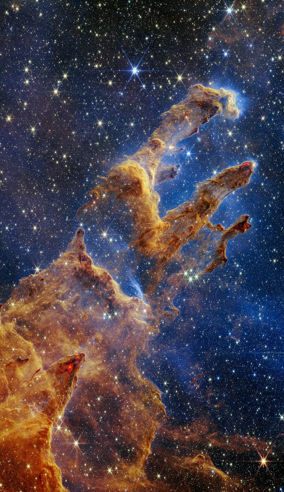 The Pillars of Creation are set off in a kaleidoscope of color in NASA’s JWST's near-infrared-light view. The pillars look like arches and spires rising out of a desert landscape, but are filled with semi-transparent gas and dust, and ever changing. This is a region where young stars are forming – or have barely burst from their dusty cocoons as they continue to form.