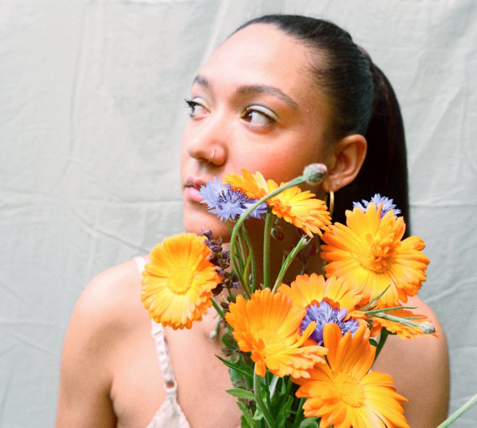 A woman with long, dark hair pulled into a pony tail looks to her right while holding a bouquet of orange and purple flowers.