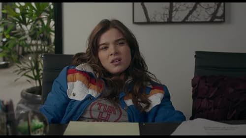 Hailee Steinfeld in The Edge of Seventeen. She is wearing an oversized jacket and slouching. Her hair is a mess, and she has an annoyed expression on her face.