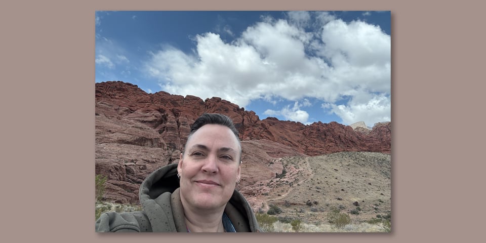 Leoh stands in front of Red Rock mountain with a blue sky and puffy white clouds behind him