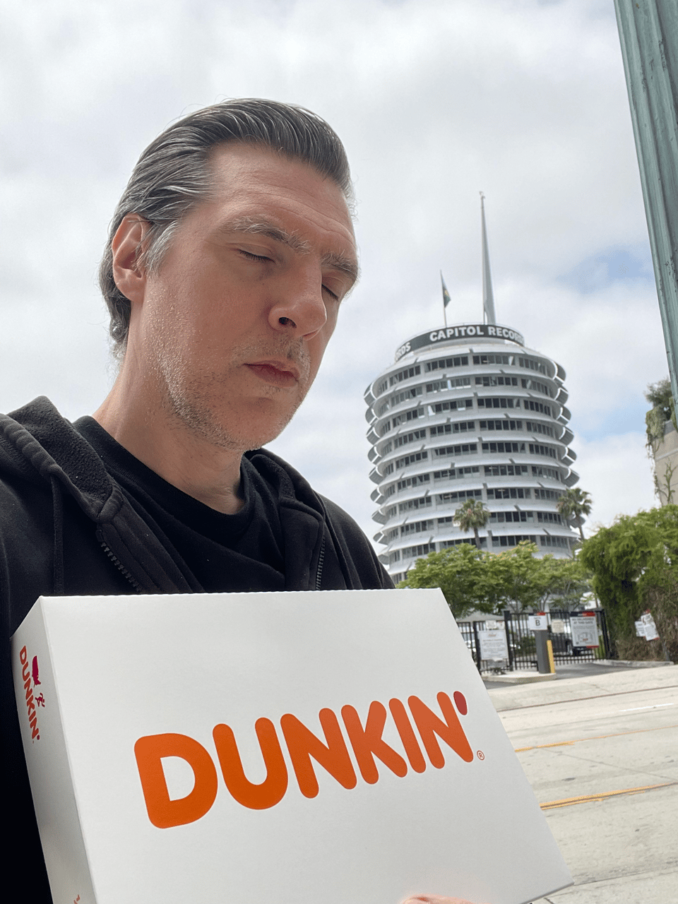 A middle-aged man looks very tired holding a box of donuts
