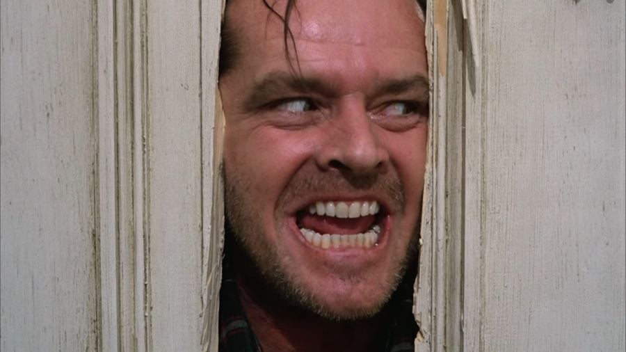Jack Torrance sticking his head through a wide hole he just cut into a wooden door with his axe. He looks wild, his mouth leering open as he says “Here’s Johnny!”