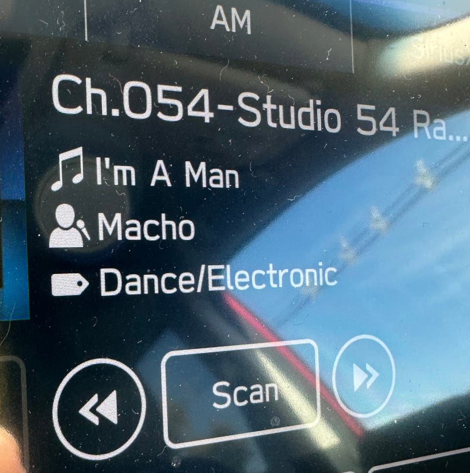 Photo of a car's display showing a Sirius radio channel playing I'M A MAN by Macho, on the Studio 54 channel