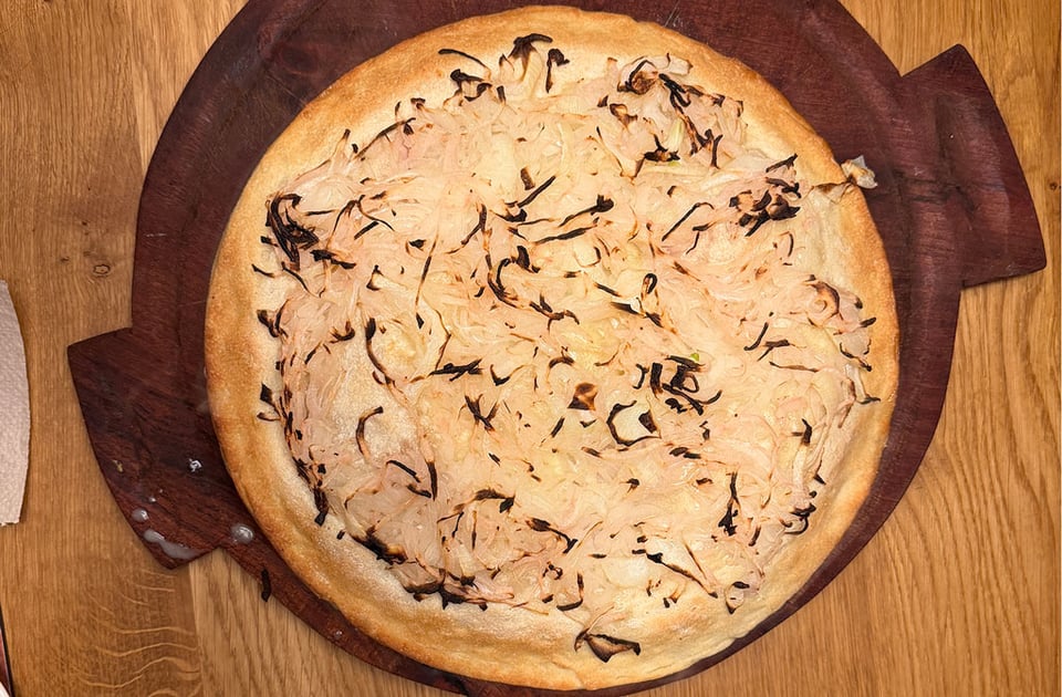 A fugazetta pizza covered in onions is on a round wooden serving platter on a wooden table.