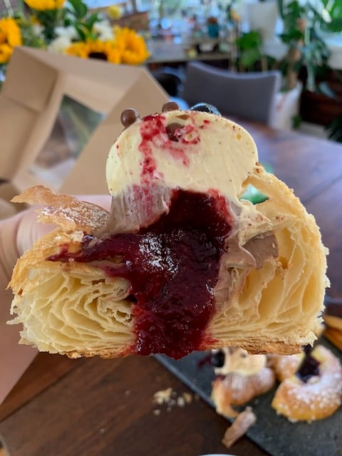 A cross section of a croissant stuffed with red cherry jam and brown chocolate mousse is held up to the camera