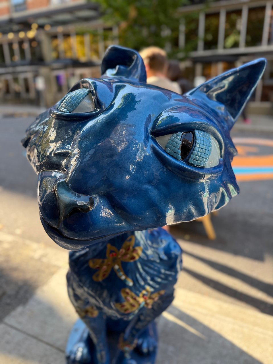 A close-up of a stylized cat sculpture covered with paint and mosaic tiles