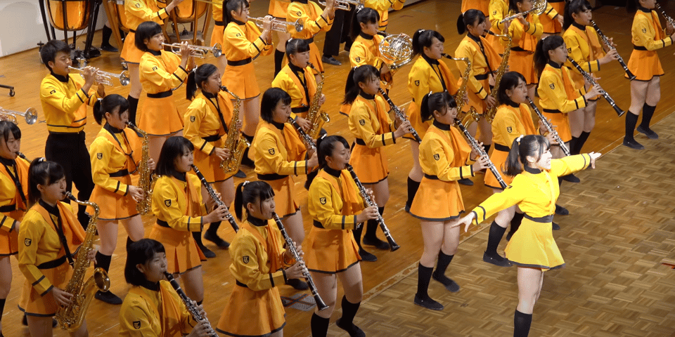 A screenshot of the band dancing and dressed in orange.