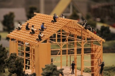 The frame of a wooden barn with roughly 15 Amish workers with tools building the structure.  From https://flic.kr/p/aiosyg with license CC BY-NC-SA 2.0