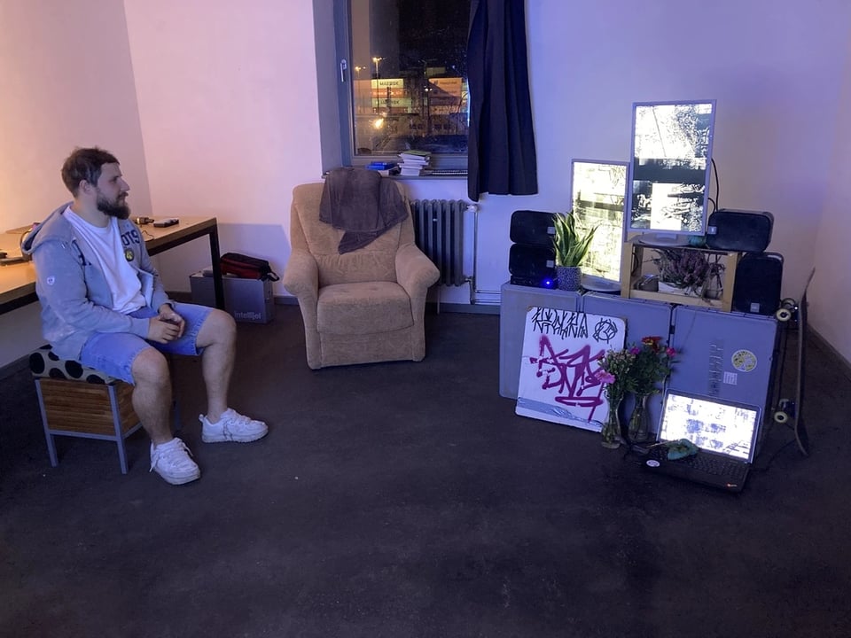 a room with easy chair, a person sitting, and an art installation with multiple screens, plants