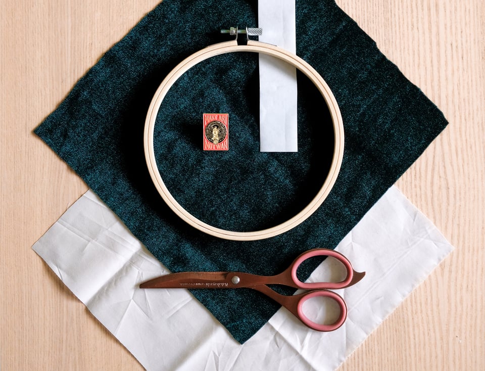 A photo of the materials, neatly organised. Scissors, an embroidery hoop, two types of fabric, dark velvet and white cotton, a pin, and fabric tape.
