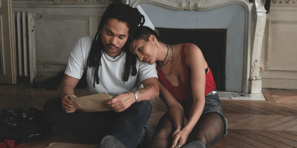 Twin siblings look at old photos in an empty apartment.