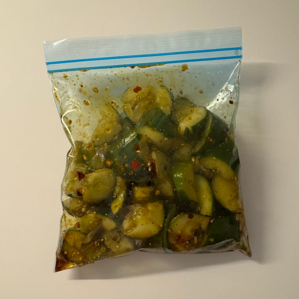 Bag of cucumber salad — smashed cucumbers marinating with chili and sauce in a plastic bag.