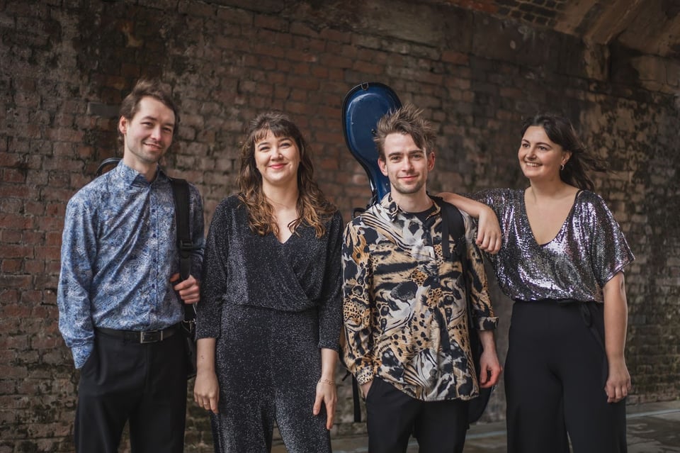 Four performers in a relaxed pose against a dark background