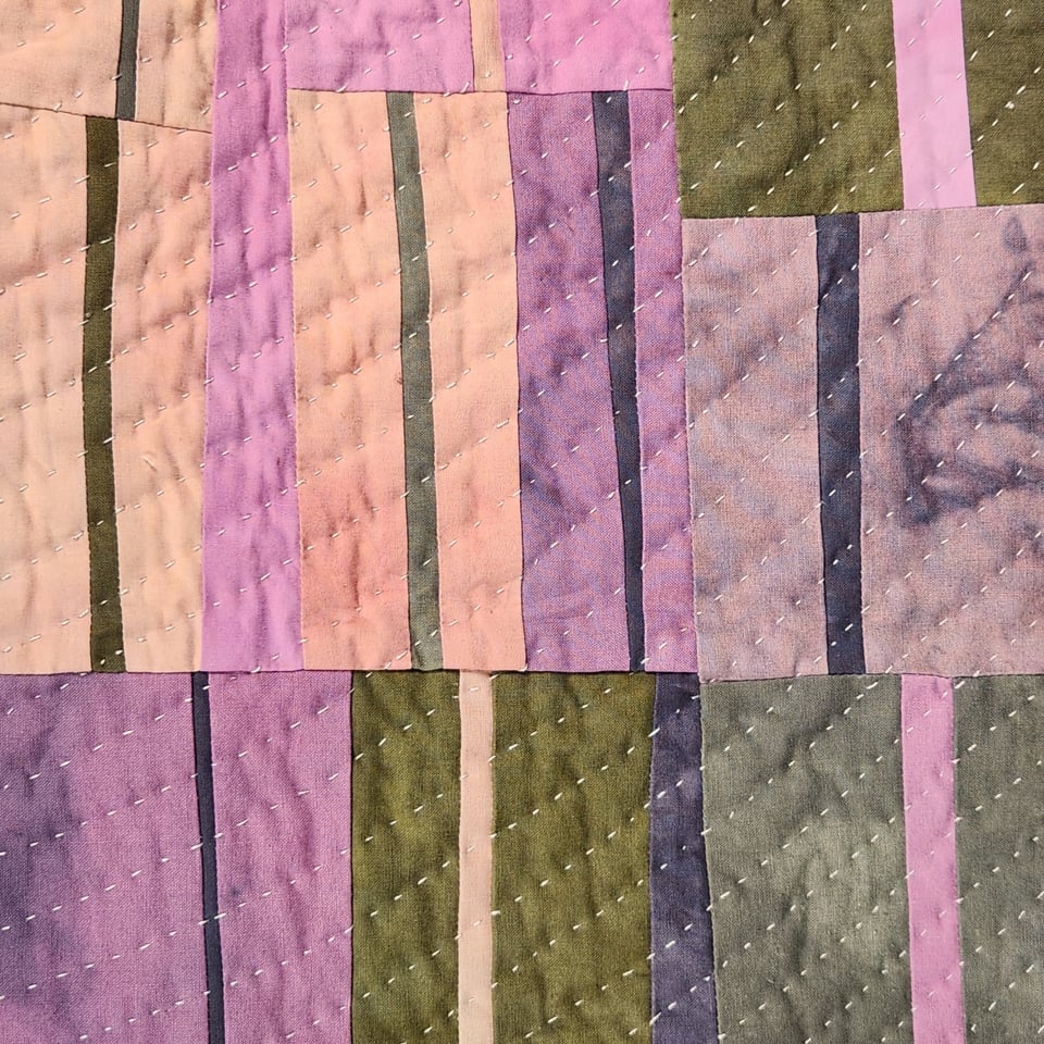 Detail view of Sarah Atlee’s patchwork quilt titled Arabesque I. The quilt is made from hand-dyed fabrics in pink, orange, grey, purple, and yellow green.