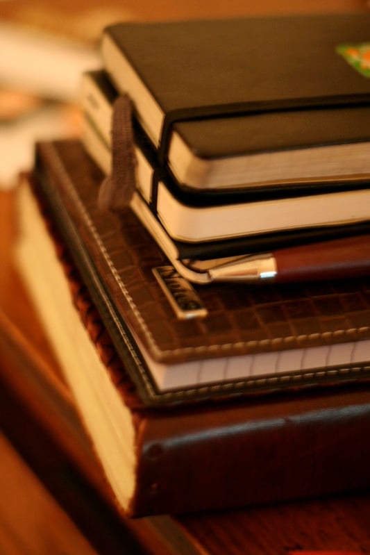 A stack of leather-bound notebooks sitting on a dark hardwood table.
