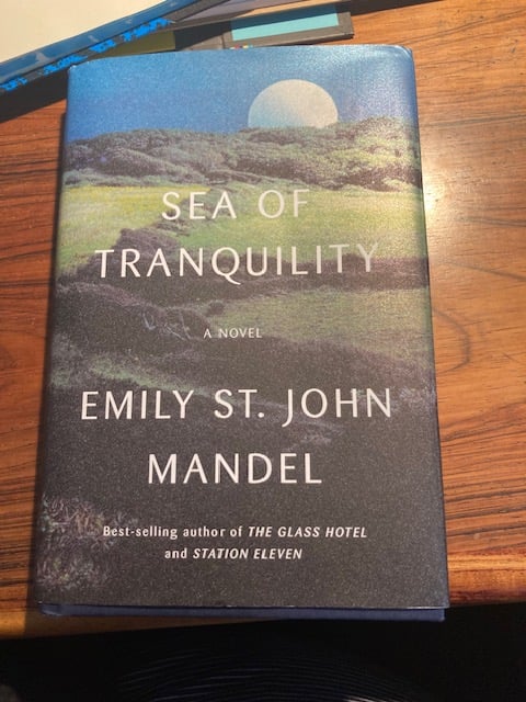 hardcover copy of Sea of Tranquility by emily st john mandel - image of a green land with a moon rising on the horizon