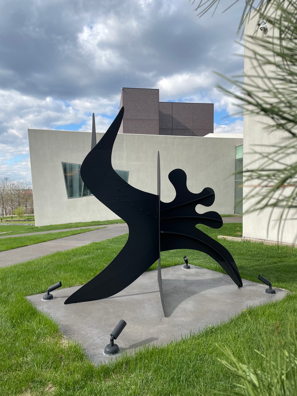 A sculpture on a grassy hillside. Made of black metal. Sharp, jutting shapes seem to pass through a portal and emerge on the other side flowing and rounded