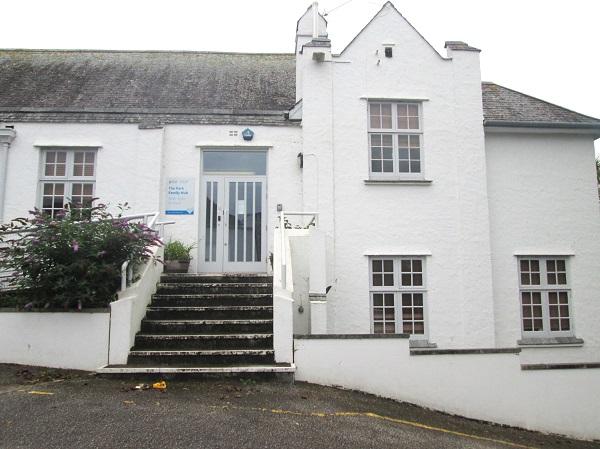 A large white rendered building on a slope. It has a pitch slate roof and a gable on one part. It's not overly special.