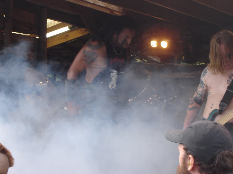 The singer from Gorgon Vomit moshes on stage as dry ice envelops the outdoor stage, the bass player to the right with Big Riffs