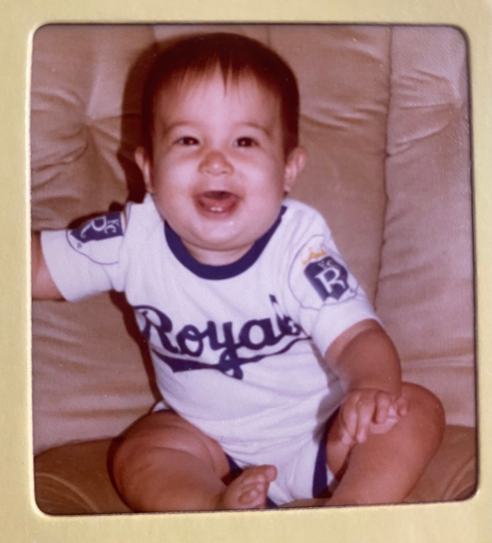 a photo of Kandace as a baby in a white Royals baseball onesie where she's smiling